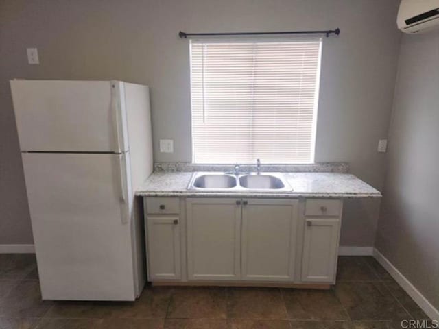 kitchen with white fridge, white cabinetry, an AC wall unit, and sink