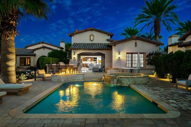 back house at twilight featuring a patio area, a swimming pool with hot tub, a bar, and an outdoor structure