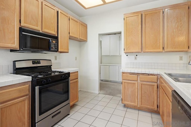 kitchen with sink, tile countertops, light brown cabinetry, light tile patterned floors, and appliances with stainless steel finishes