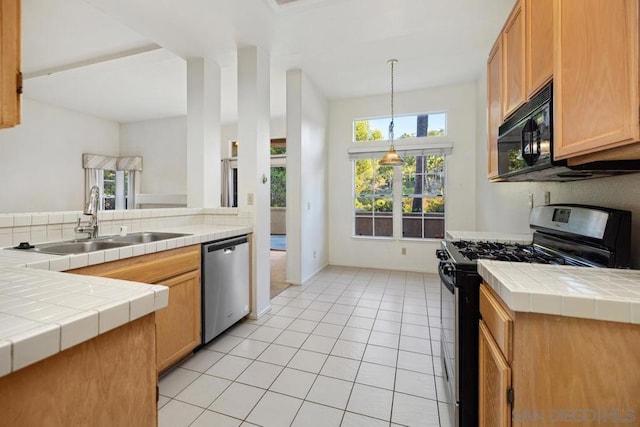 kitchen featuring tile countertops, hanging light fixtures, sink, light tile patterned floors, and appliances with stainless steel finishes