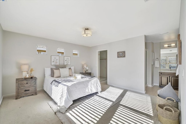 bedroom featuring a closet, ensuite bath, light colored carpet, sink, and a walk in closet