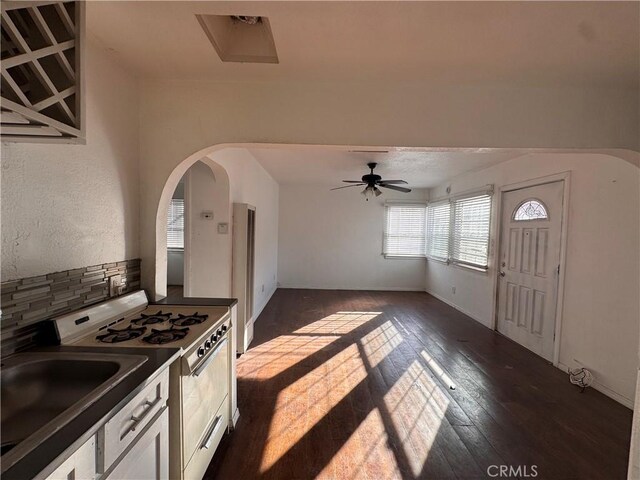 kitchen with white stove, ceiling fan, decorative backsplash, dark hardwood / wood-style floors, and white cabinets