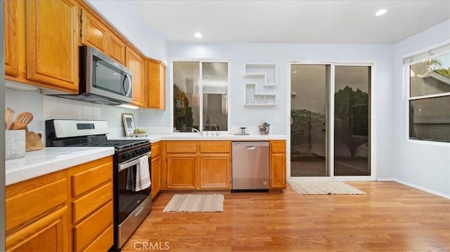 kitchen featuring backsplash, tile countertops, sink, light hardwood / wood-style flooring, and appliances with stainless steel finishes