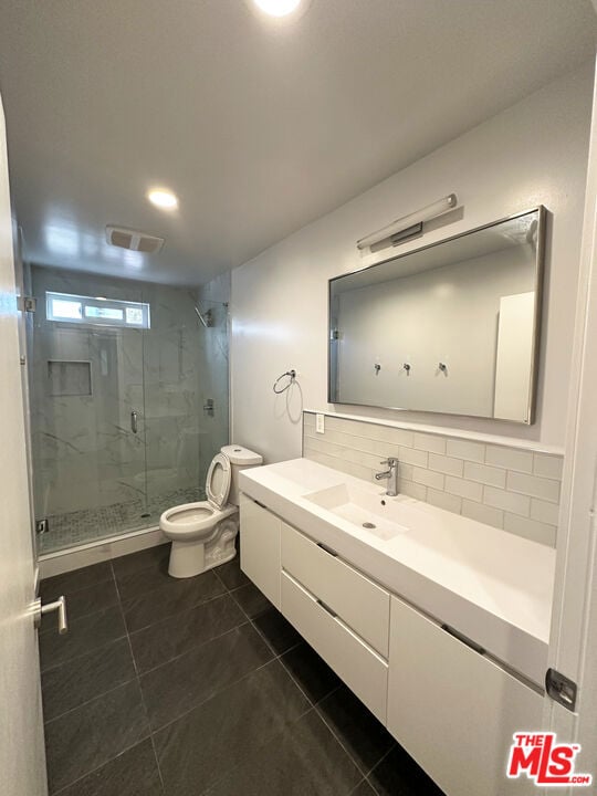 bathroom featuring tile patterned flooring, a shower with door, vanity, tasteful backsplash, and toilet