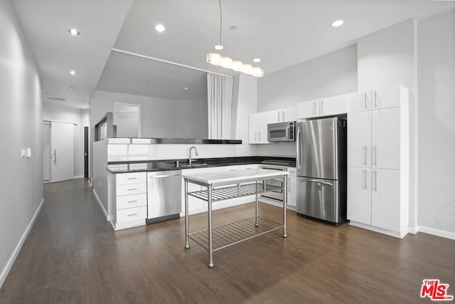 kitchen featuring dark wood-type flooring, white cabinets, sink, hanging light fixtures, and appliances with stainless steel finishes