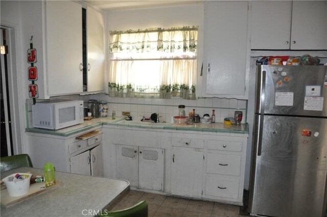 kitchen featuring sink, white cabinetry, tasteful backsplash, and stainless steel refrigerator