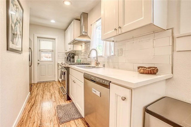 kitchen with backsplash, sink, appliances with stainless steel finishes, white cabinets, and wall chimney exhaust hood