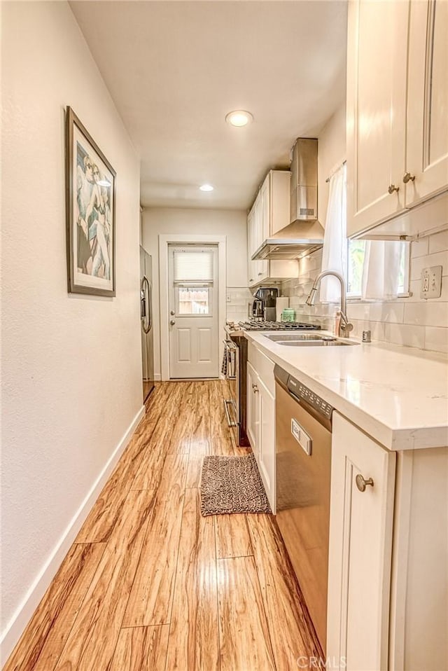 kitchen featuring tasteful backsplash, sink, light wood-type flooring, appliances with stainless steel finishes, and wall chimney exhaust hood