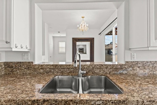 kitchen featuring white cabinets, dark stone counters, sink, and an inviting chandelier