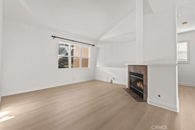 unfurnished living room featuring a fireplace, plenty of natural light, light wood-type flooring, and vaulted ceiling