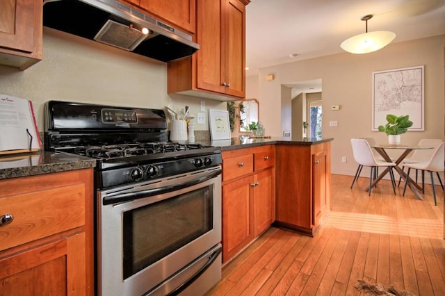 kitchen with gas range, decorative light fixtures, light wood-type flooring, dark stone countertops, and range hood