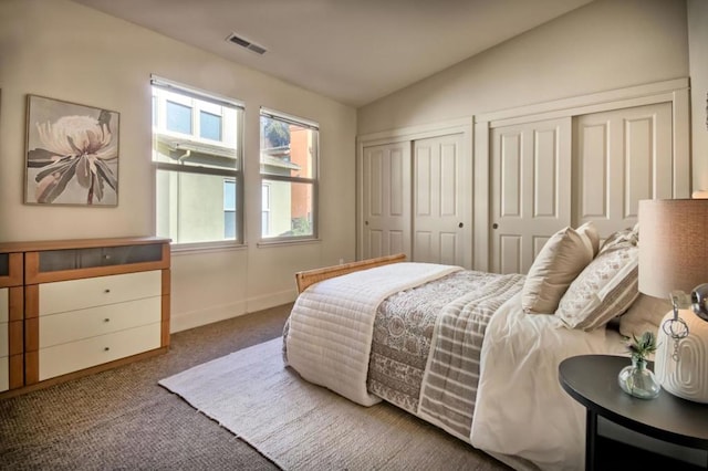 carpeted bedroom featuring multiple closets and vaulted ceiling