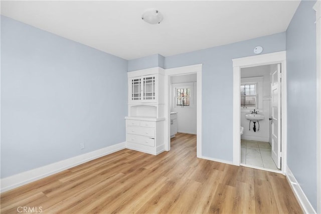 unfurnished bedroom featuring sink, light hardwood / wood-style floors, and ensuite bath