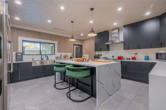 kitchen with wall chimney exhaust hood, a center island, pendant lighting, crown molding, and sink