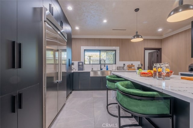 kitchen featuring built in fridge, light stone countertops, hanging light fixtures, and ornamental molding