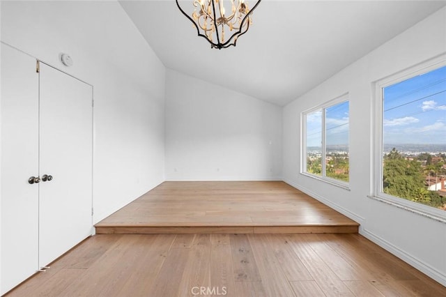 unfurnished room featuring lofted ceiling, a notable chandelier, and light hardwood / wood-style floors