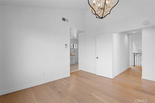 spare room with lofted ceiling, a notable chandelier, and light hardwood / wood-style floors