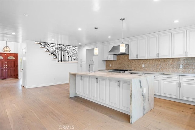 kitchen with white cabinetry, wall chimney exhaust hood, and an island with sink