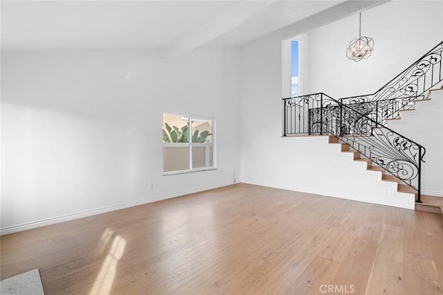 unfurnished living room featuring a notable chandelier, beamed ceiling, a high ceiling, and hardwood / wood-style floors