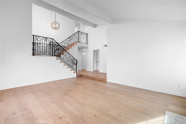 unfurnished living room featuring a high ceiling, wood-type flooring, beamed ceiling, and an inviting chandelier