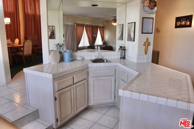 kitchen featuring tile counters, light tile patterned floors, kitchen peninsula, and sink