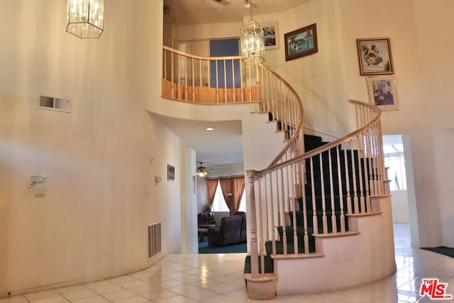 stairs with tile patterned floors, ceiling fan with notable chandelier, and a towering ceiling