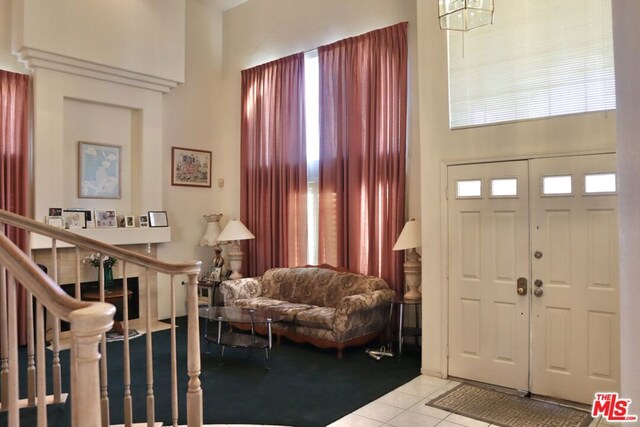 tiled entrance foyer with a notable chandelier, a towering ceiling, and a healthy amount of sunlight