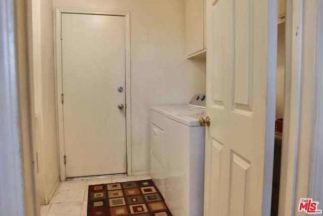 clothes washing area featuring washing machine and dryer, light tile patterned flooring, and cabinets