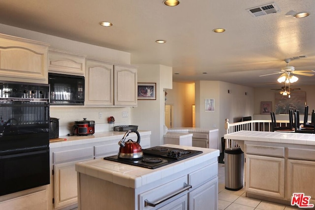 kitchen with ceiling fan, tile counters, a center island, light tile patterned flooring, and black appliances