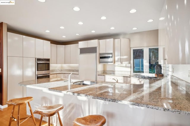 kitchen featuring stainless steel appliances, a kitchen bar, light stone countertops, and kitchen peninsula