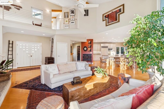 living room featuring a high ceiling, light wood-type flooring, and ceiling fan