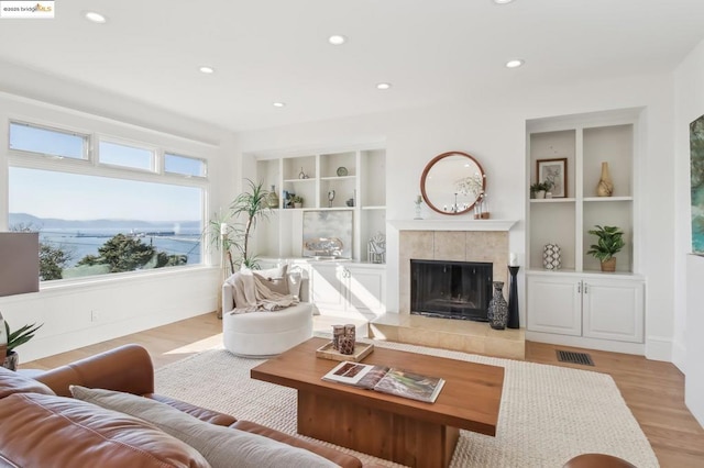 living room with a water view, built in features, a fireplace, and light hardwood / wood-style flooring