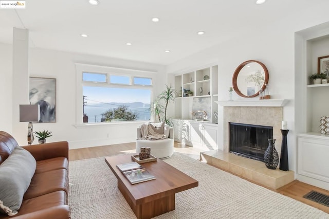 living room with a tiled fireplace, built in features, and light hardwood / wood-style floors