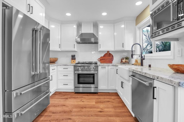 kitchen featuring white cabinetry, wall chimney exhaust hood, high quality appliances, light stone counters, and sink