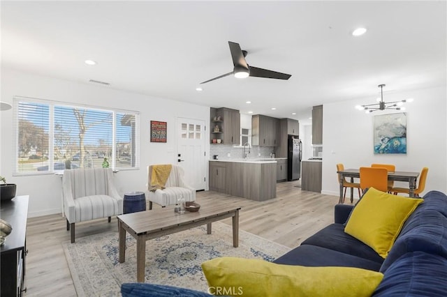 living room featuring light wood-type flooring, sink, and ceiling fan with notable chandelier