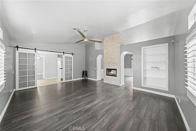 unfurnished living room featuring vaulted ceiling, a wealth of natural light, a barn door, and built in shelves