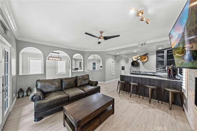 living room with ceiling fan, a tiled fireplace, and ornamental molding