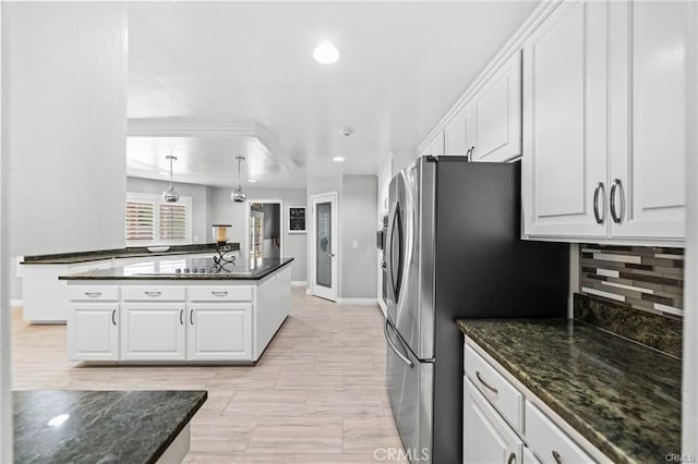 kitchen featuring white cabinetry, stainless steel fridge, decorative backsplash, hanging light fixtures, and dark stone counters