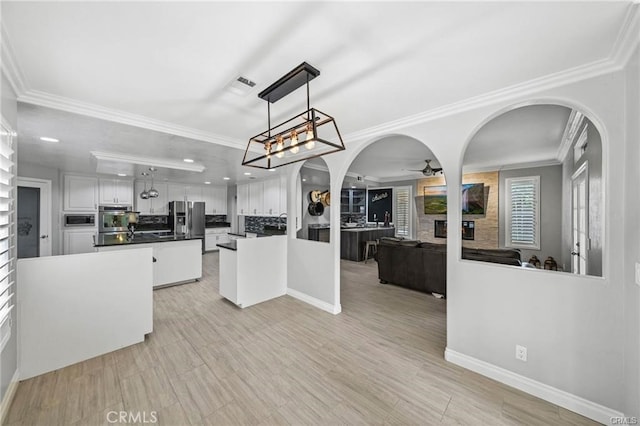 kitchen with pendant lighting, white cabinets, a center island, appliances with stainless steel finishes, and ornamental molding