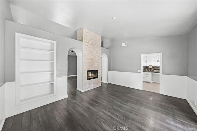 unfurnished living room featuring built in shelves, dark hardwood / wood-style flooring, lofted ceiling, and a fireplace