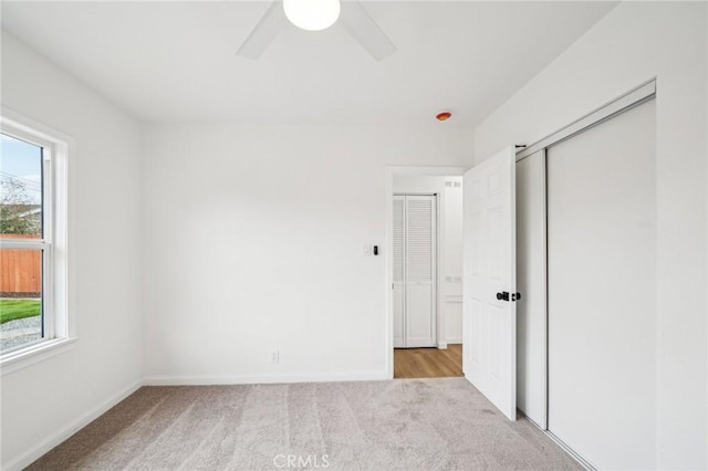 unfurnished bedroom with ceiling fan, light colored carpet, a closet, and multiple windows