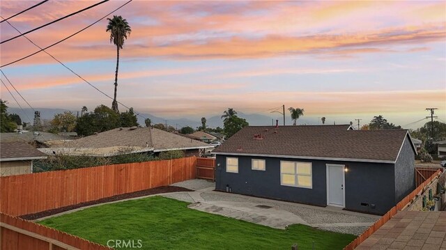 back house at dusk featuring a patio area and a lawn