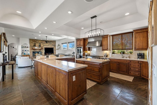 kitchen featuring a fireplace, pendant lighting, light stone countertops, a large island, and ventilation hood