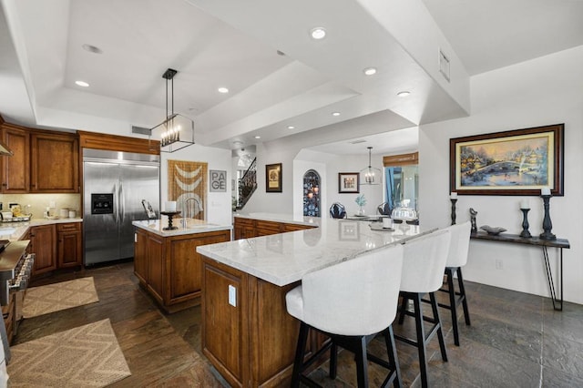 kitchen featuring a large island, built in refrigerator, a tray ceiling, decorative light fixtures, and a breakfast bar