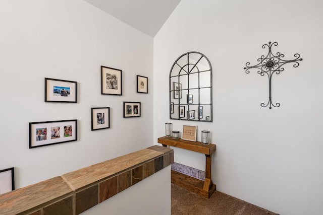 hallway with vaulted ceiling and dark colored carpet