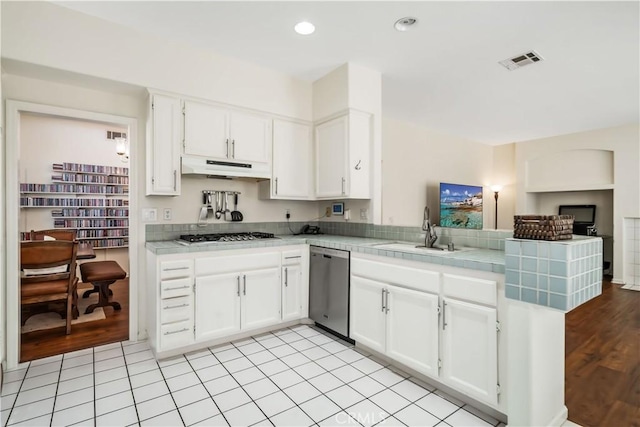 kitchen with kitchen peninsula, sink, white cabinetry, appliances with stainless steel finishes, and tile counters