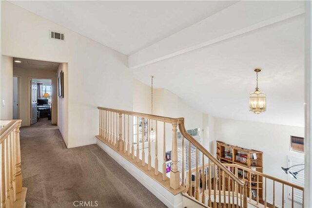 corridor with lofted ceiling with beams, an inviting chandelier, and dark carpet