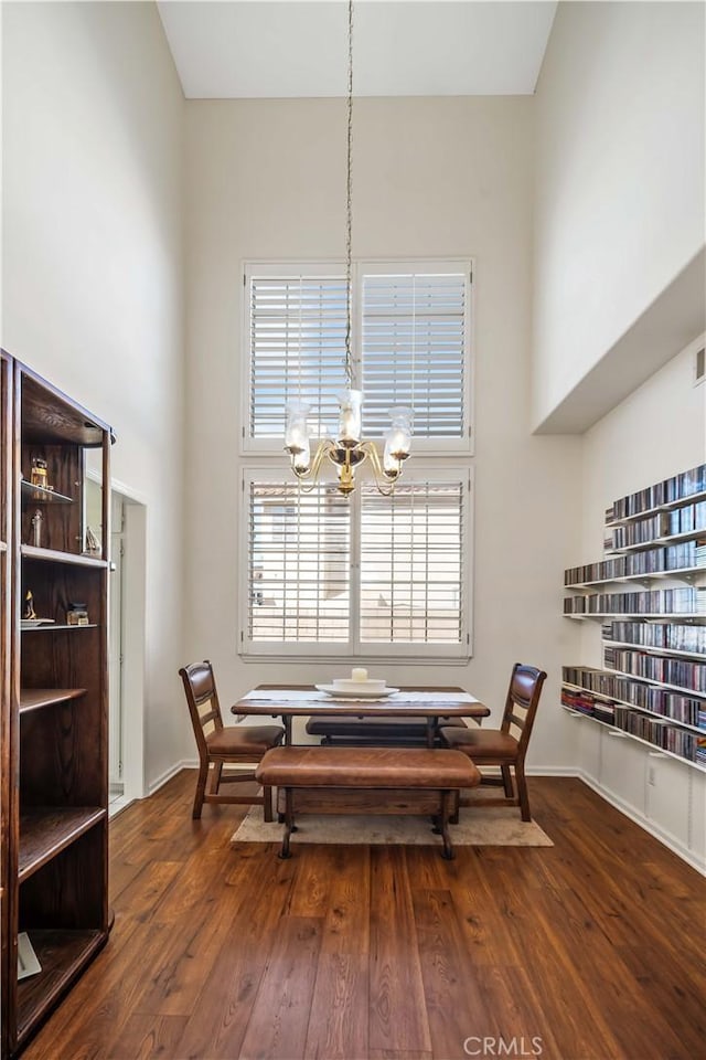 dining space with a towering ceiling, a chandelier, and dark hardwood / wood-style floors