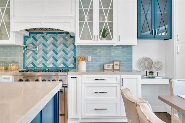 kitchen featuring decorative backsplash, stainless steel stove, white cabinets, and ventilation hood