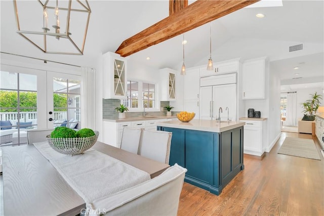 kitchen with an island with sink, paneled fridge, pendant lighting, white cabinets, and sink